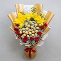 Bouquet of flowers with yellow lilies, red roses, and Ferrero rocher chocolate on a gray background